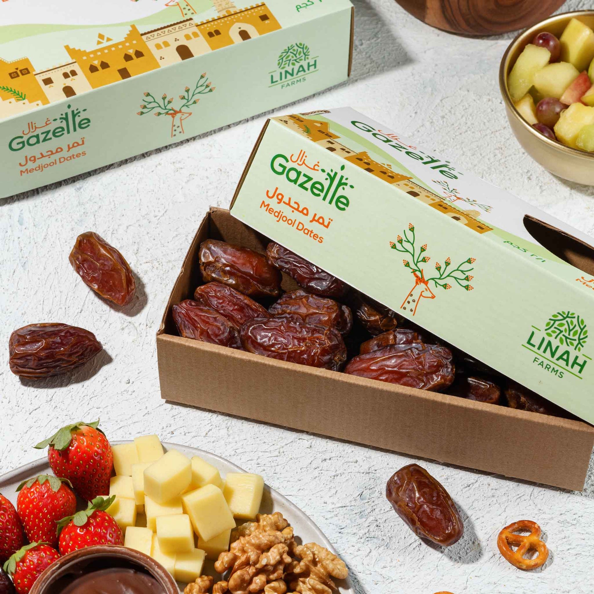 Pack of Gazelle Medjool dates with medjool dates lying around and a small charcuterie board on the side